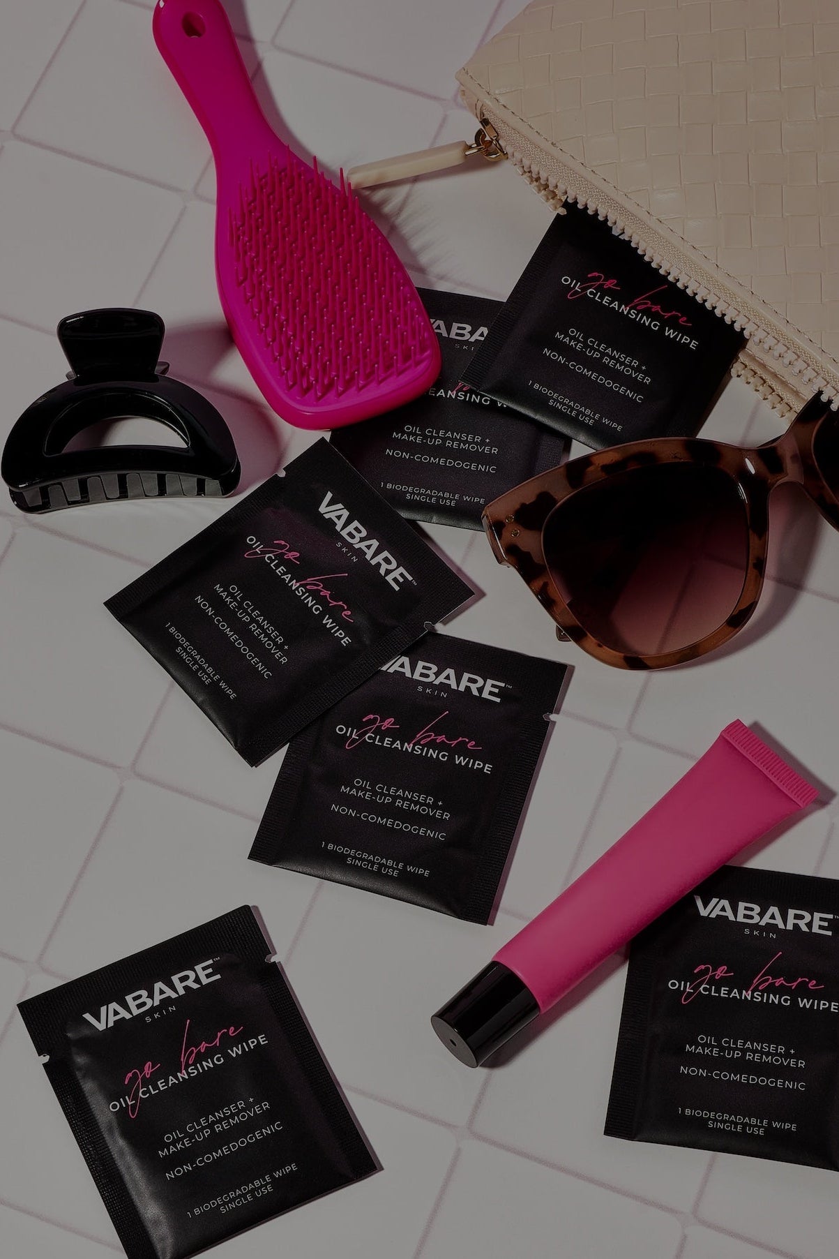 Vabare oil cleansing wipes with a pink brush, black tool, and sunglasses on a light background