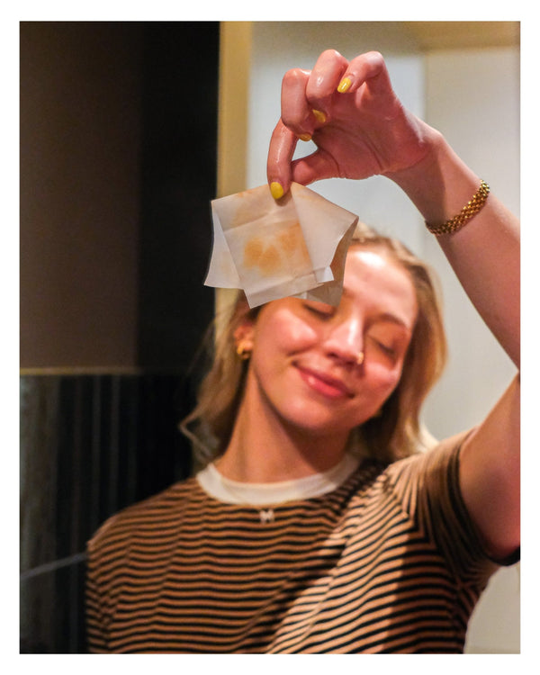 Person holding a used VABARE oil cleansing wipe up to their face with a blurred background
