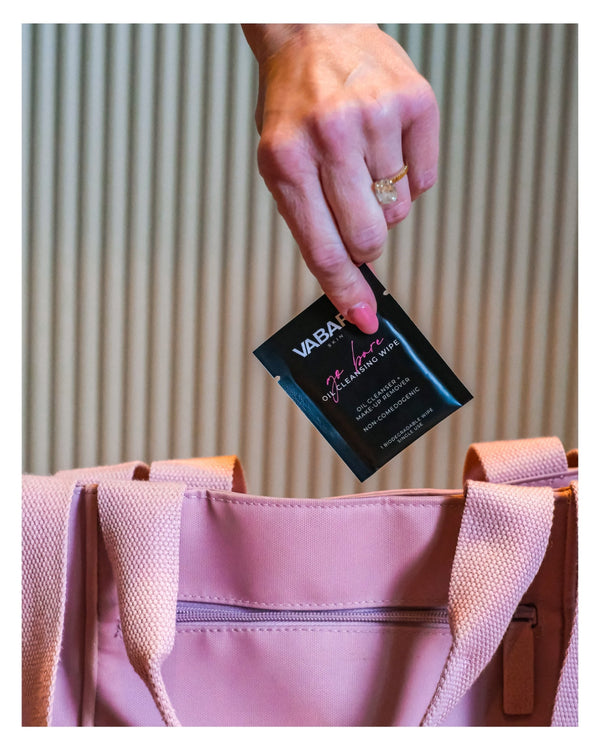 Hand pulling a VABARE Skin oil cleansing makeup remover wipe out of a pink bag with a neutral background