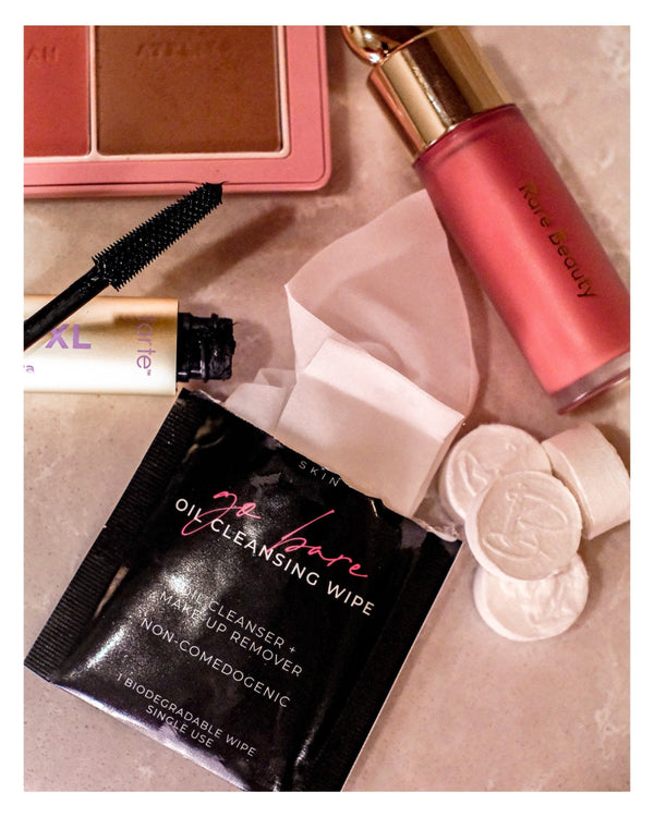 Makeup products including a compact, mascara, and VABARE Skin oil cleansing wipes on a beige surface.